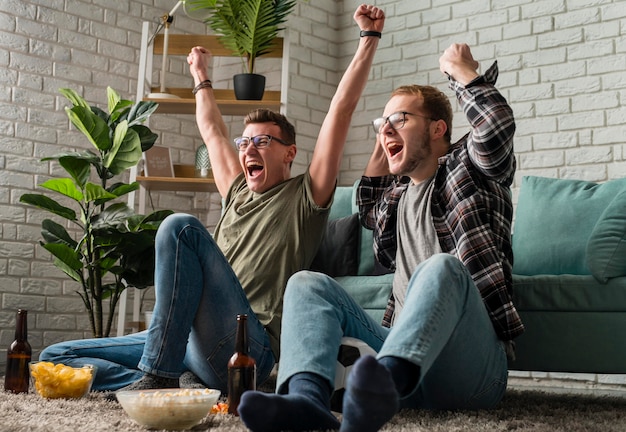 Foto zwei fröhliche männliche freunde, die zusammen sport im fernsehen schauen, während sie snacks und bier trinken