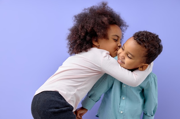 Zwei fröhliche schwarze amerikanische Geschwister Schwester küssen ihren Bruder isoliert auf violettem Hintergrund portra