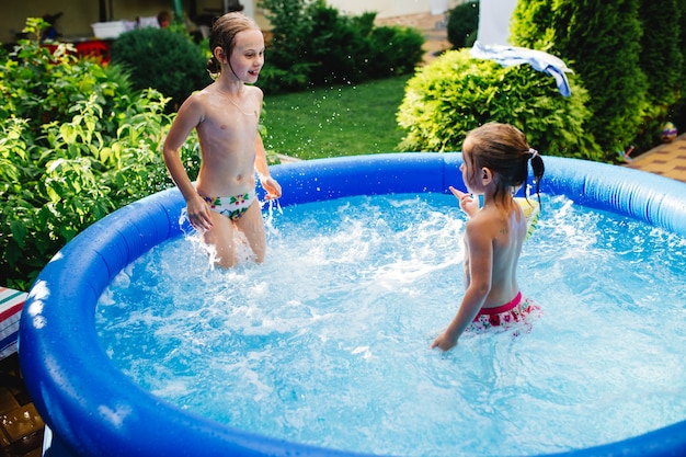 Foto zwei fröhliche süße kleine schwestern, die spielen und spaß haben, planschen und im aufblasbaren pool im hinterhof springen.