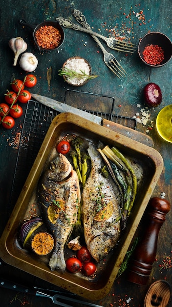 Zwei gebackene Dorado-Fische mit Spargel und Gemüse in einem Metallbehälter. Ansicht von oben. Freier Kopienraum. Auf einem schwarzen Steinhintergrund.