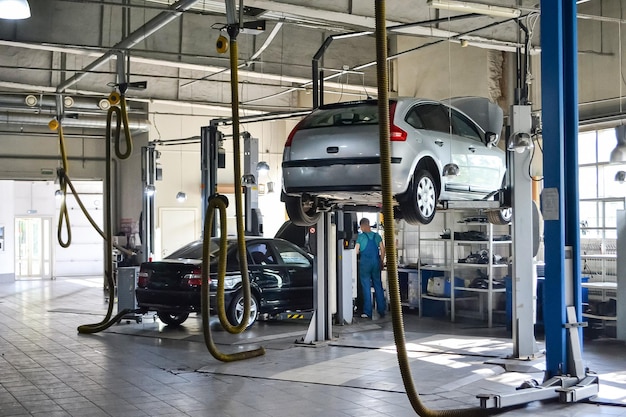 Zwei Gebrauchtwagen mit offener Motorhaube, die auf einer Hebebühne angehoben wurden, um das Fahrgestell und den Motor in einer Kfz-Werkstatt zu reparieren