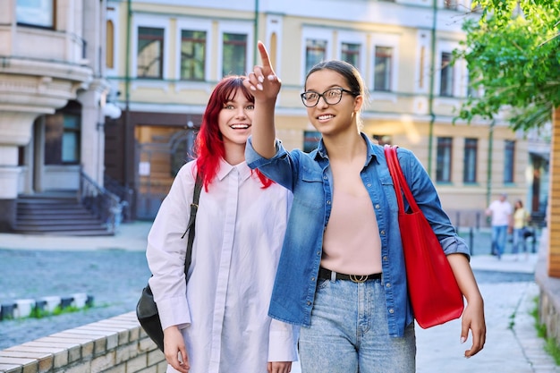 Zwei gehende, sprechende, lachende Mädchen im Teenageralter, die die Straße der Stadt hinuntergehen