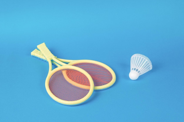 Zwei gelbe Badmintonschläger und ein Federball auf blauem Grund