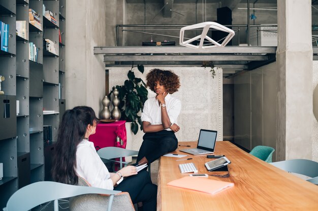 Zwei gemischtrassige junge Geschäftsfrauen, die Sitzung im modernen Büro haben