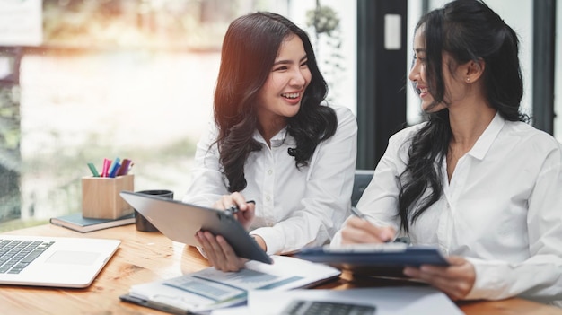 Zwei Geschäftsfrauen arbeiten mit Tablet und Laptop zusammen, um eine Bewertung am Arbeitsplatz zu berechnen