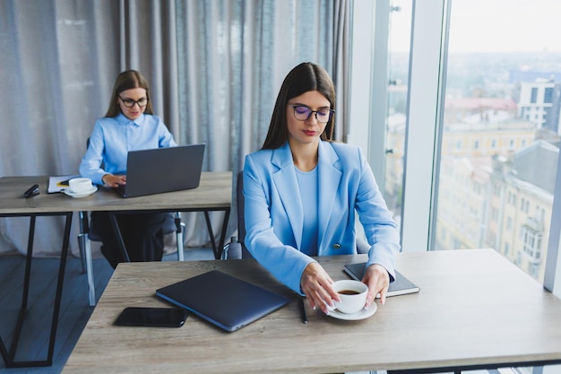 Zwei Geschäftsfrauen bei der Arbeit Kluge Angestellte mit Brille, erfolgreiche Freiberuflerin in einem Jackett-Workflow in einem Büro mit großen Fenstern