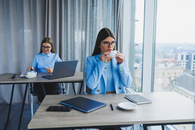 Zwei Geschäftsfrauen bei der Arbeit Kluge Angestellte mit Brille, erfolgreiche Freiberuflerin in einem Jackett-Workflow in einem Büro mit großen Fenstern