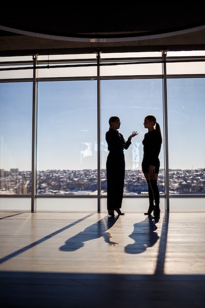 Zwei Geschäftsfrauen, die den Blick auf die Stadt genießen und sich unterhalten, während sie am großen Fenster im Büro stehen