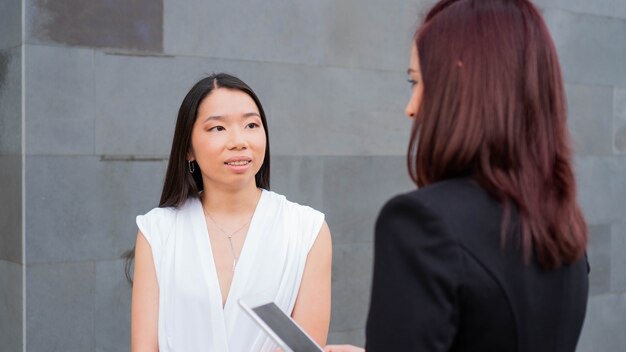 Zwei Geschäftsfrauen, die in ihrem Arbeitsbereich sprechen Eine Chefin mit ihrem Tablet asiatischer Arbeiter