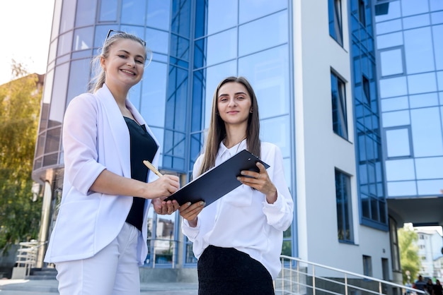 Zwei Geschäftsfrauen, die vor dem Bau eines großen Bürozentrums einen Vertrag im Freien unterzeichnen