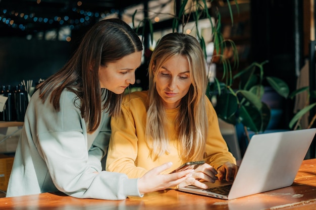 Zwei Geschäftsfrauen diskutieren Online-Inhalte und benutzen Telefon und Laptop