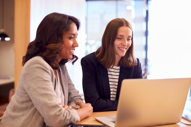 Zwei Geschäftsfrauen mit Laptop, die gemeinsam an einem Projekt im Büro arbeiten