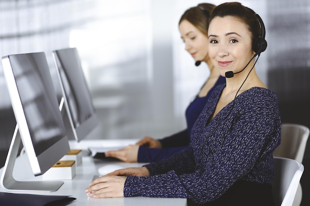 Zwei Geschäftsfrauen unterhalten sich mit den Kunden über Headsets, während sie in einem modernen Büro am Schreibtisch sitzen. Verschiedene Menschen gruppieren sich in einem Call Center. Telemarketing und Kundenservice.