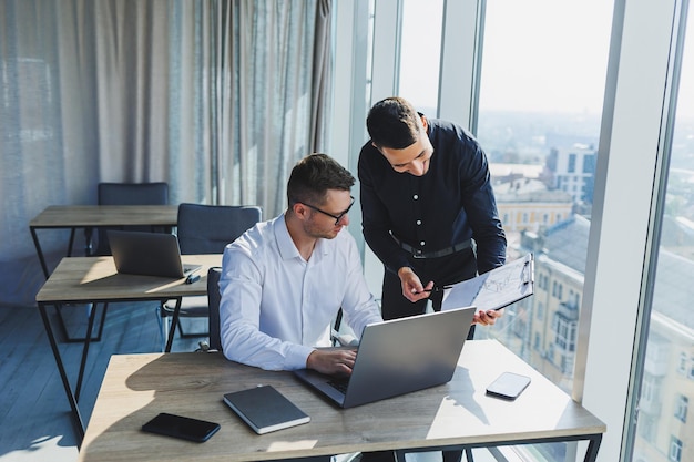 Zwei Geschäftsleute erstellen ein Projekt, während sie während eines Meetings in einem modernen Sitzungssaal auf den Laptop-Bildschirm schauen Arbeitsprozess in einem modernen Büro