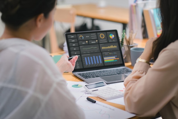 Zwei Geschäftsleute oder ein Buchhalterteam analysieren Datendiagramme, Diagramme und ein Dashboard auf einem Laptop-Bildschirm, um einen statistischen Bericht vorzubereiten und finanzielle Daten in einem Büro zu besprechen