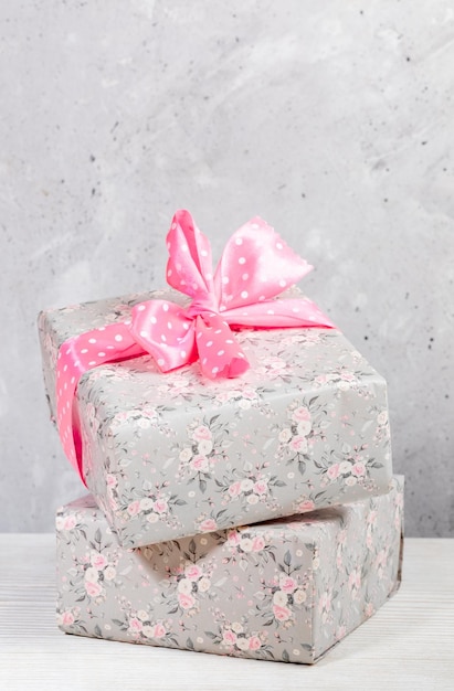 Zwei Geschenkboxen in grauem Blumenpapier mit rosa Tupfenschleife auf neutralem Hintergrund