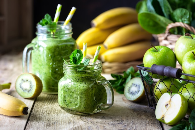 Zwei gesunde grüne Smoothies mit Spinat, Banane, Apfel, Kiwi und Minze im Glas und Zutaten. Entgiftung, Diät, gesundes, vegetarisches Lebensmittelkonzept.