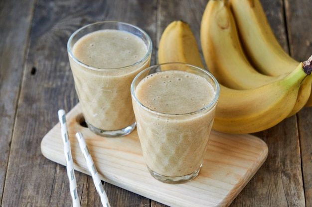 Zwei Gläser Bananen-Smoothie auf einem Holzbrett