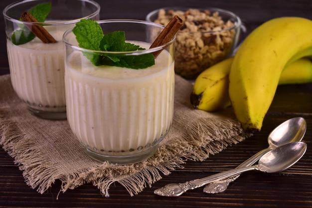 Zwei Gläser Bananen-Zimt-Joghurt auf dunklem Holzhintergrund.