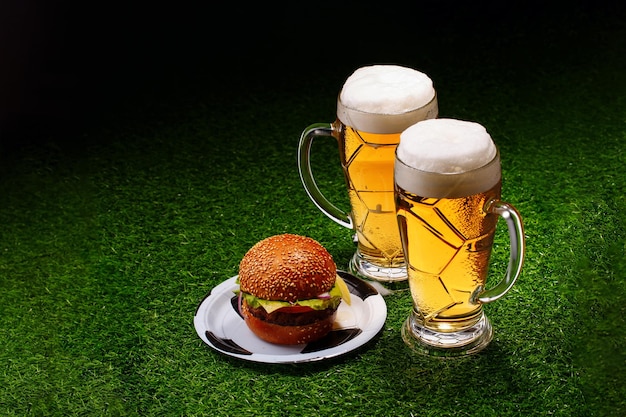 Zwei Gläser Bier und Hamburger auf grünem Gras