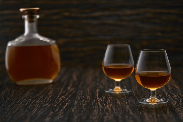 Zwei Gläser Brandy oder Cognac und Flasche auf einem Holztisch.