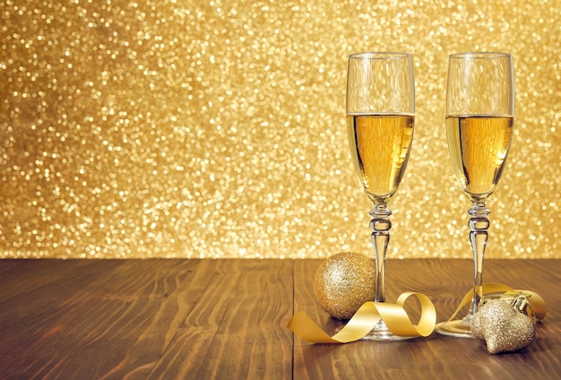 Zwei Gläser Champagner auf einem braunen Holztisch mit Weihnachtsdekoration und unscharfem Goldhintergrund