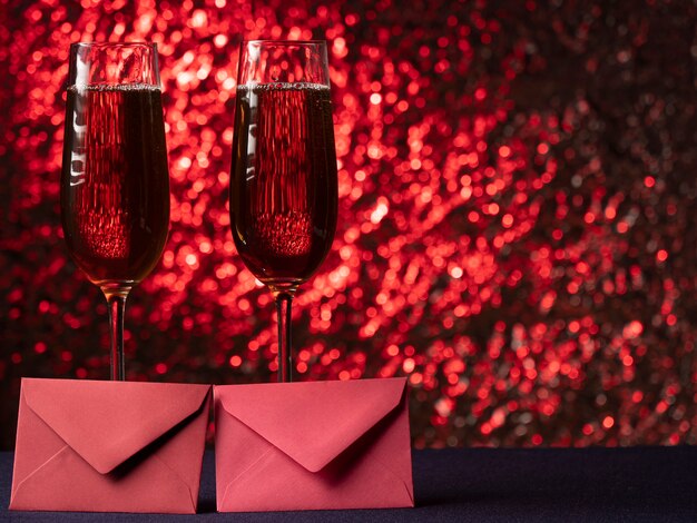 Zwei Gläser Champagner stehen auf einer blauen Oberfläche miteinander und davor befinden sich zwei rosa Karten auf einem rosa