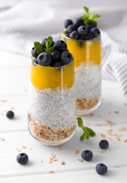 Zwei Gläser Chia-Pudding mit Blaubeeren, Mango-Mousse und Hafer-Müsli auf dem Küchentisch.