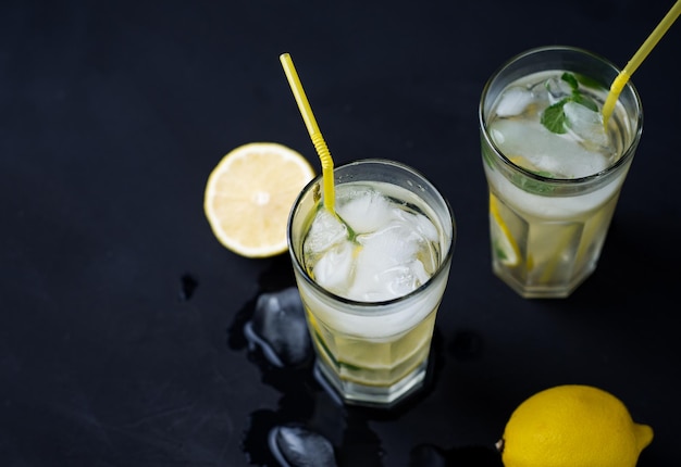 Zwei Gläser erfrischende Sommer-Zitronen-Minz-Limonade mit Eis auf dem schwarzen Tisch