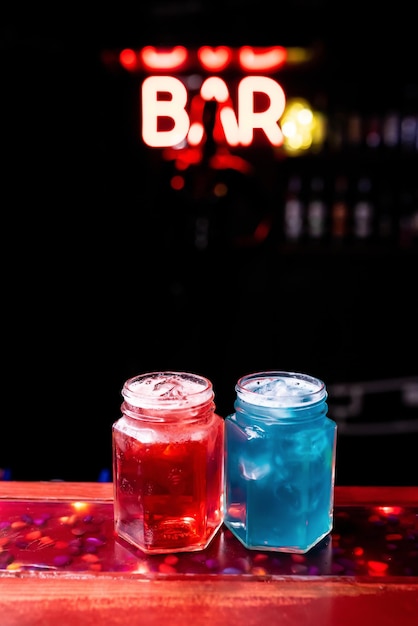 Zwei Gläser in Form von Dosen mit einem roten und blauen Cocktail in einer Nachtclubbar Nachtleben im Clubleben Ausgezeichnete Cocktails servieren