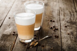 Foto zwei gläser latte kaffeebohnen und löffel om pld holztisch.