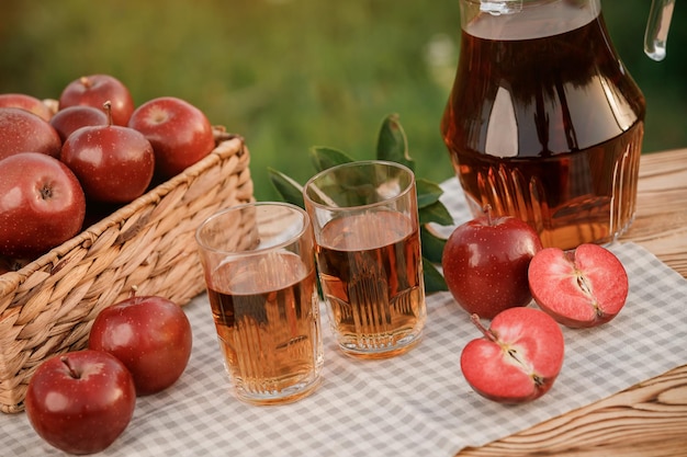 Zwei Gläser mit Apfelsaft und Korb mit Äpfeln auf Holztisch mit natürlichem Obstgartenhintergrund Vegetarische Fruchtzusammensetzung