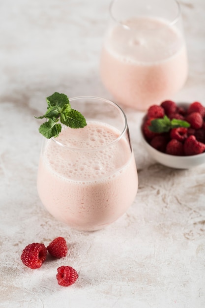 Zwei Gläser mit einem Lassi-Getränk mit Himbeeren, Minze und einer Bambusröhre auf hellem Hintergrund. Vertikale Ausrichtung. Ansicht von oben. Indisches traditionelles Erfrischungsgetränk.