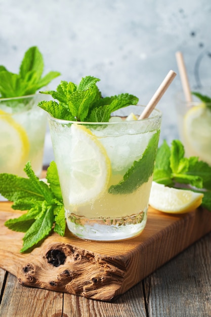 Zwei Gläser mit Limonade oder Mojito-Cocktail mit Zitrone und Minze, kaltes Erfrischungsgetränk oder Getränk mit Eis auf rustikalem blauem Hintergrund.