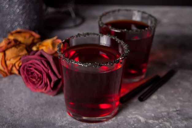 Zwei Gläser mit rotem Cocktail, getrocknete Rosen für Halloween-Party auf Dunkelheit