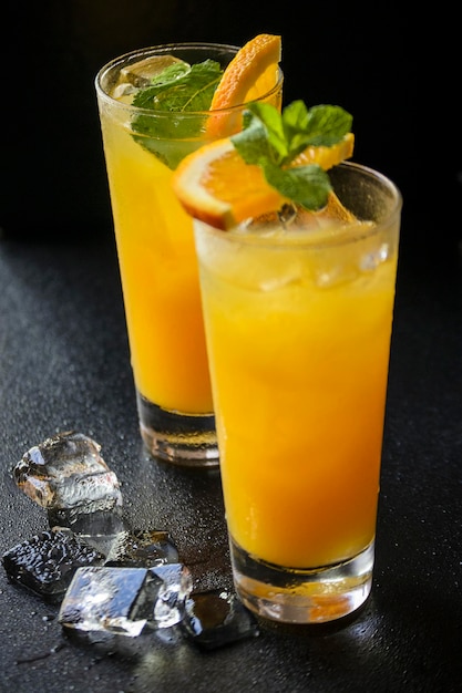 Zwei Gläser Orangengetränk mit Eiswürfeln und Minzblättern