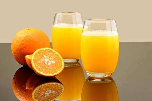 zwei Gläser Orangensaft auf einer reflektierenden dunklen Oberfläche