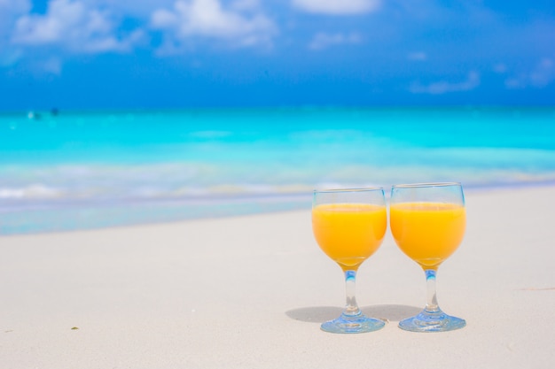 Zwei Gläser Orangensaft auf tropischem weißem Strand