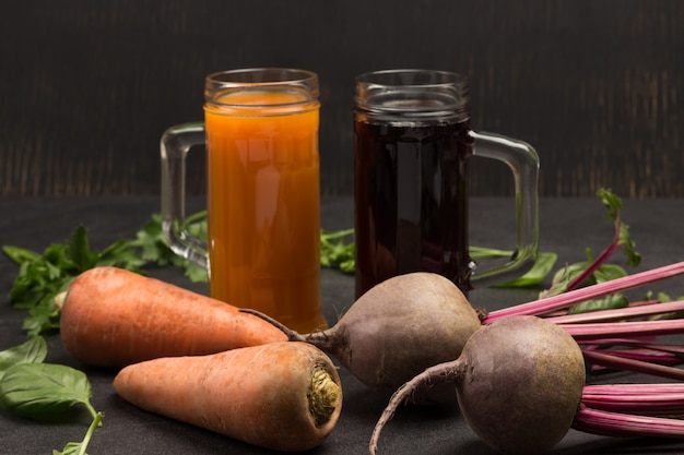 Zwei Gläser Rote Beete und Karottensaft. Wurzelgemüse aus Rüben und Karotten, Petersilie und Basilikum. Draufsicht. Schwarzer Hintergrund