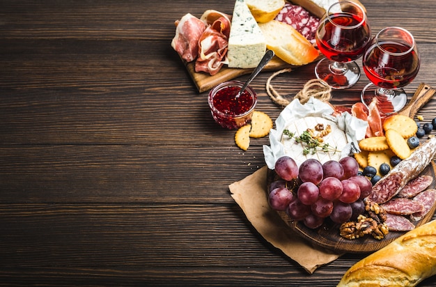 Zwei Gläser Rotwein, Holzbrett, Aufschnitt, Käse, Obst, Dip. Holzhintergrund