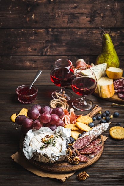 Zwei Gläser Rotwein, Holzbrett, Aufschnitt, Käse, Obst, Dip. Holzhintergrund