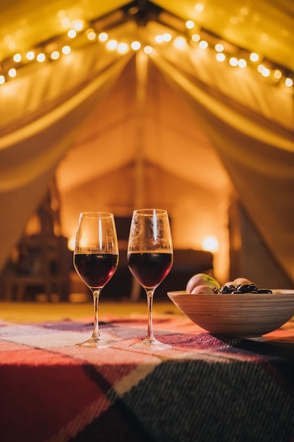 Zwei Gläser Rotwein und Teller mit Früchten stehen auf dem Hintergrund eines gemütlichen Glamping-Zeltes am Herbstabend Luxus-Campingzelt für Urlaub im Freien und Urlaub Lifestyle-Konzept