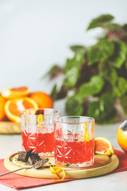 Zwei Gläser Schokoladen-Rot-Orange-Negroni, ein italienischer Cocktail, ein Aperitif, der erstmals 1919 in Florenz, Italien, gemixt wurde. Ein alkoholischer Bittercocktail, serviert mit Zutaten auf dem hellgrauen Tisch