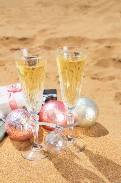 Zwei Gläser Weihnachtschampagner und Blasen mit Weihnachtsgeschenken und Dekorationen am Strand