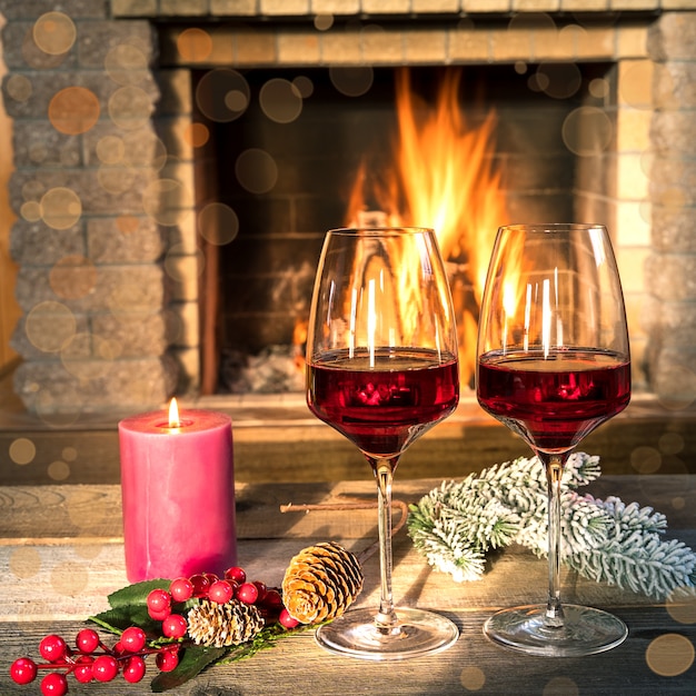 Zwei Gläser Wein und Kerze nahe gemütlichem Kamin