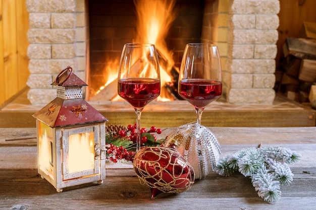 Zwei Gläser Wein und Weihnachtslaterne nahe gemütlichem Kamin im Landhaus.