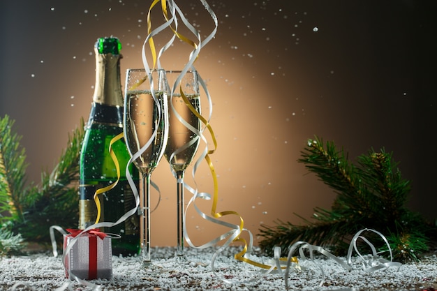 Zwei Gläser weißer Champagner, offene Flasche und Weihnachtsdekorationen