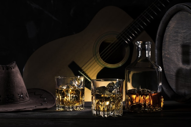 Zwei Gläser Whisky mit Eis und Cowboyhut auf Holztisch