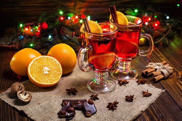 Zwei Gläser Winter wärmendes rotes heißes Getränk Weihnachtsglühwein auf hölzernem Hintergrund mit spicesorange Sliceanise und Zimtstangen