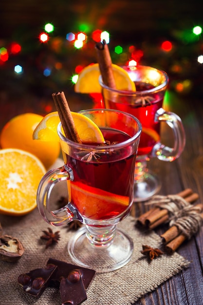 Zwei Gläser Winter wärmendes rotes heißes Getränk Weihnachtsglühwein auf hölzernem Hintergrund mit spicesorange Sliceanise und Zimtstangen